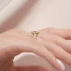 2 carat oval moissanite engagement ring worn on hand in yellow gold showing cluster side stones and slim band lifestyle view (1)