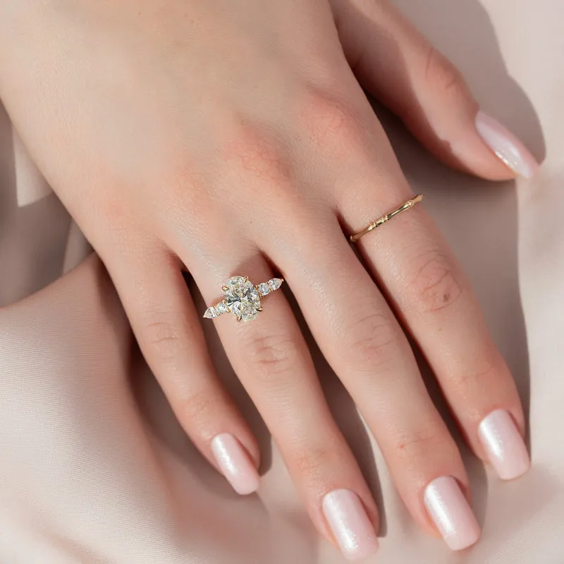 2 carat oval moissanite engagement ring worn on hand in yellow gold showing cluster side stones and slim band lifestyle view (2)