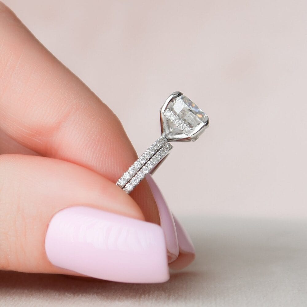 A close-up of a hand wearing a white gold engagement ring with a large, cushion-cut center stone and two diamond-encrusted bands.