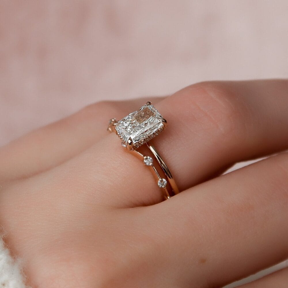 A close-up of a woman's hand showcasing a stunning radiant cut solitaire engagement ring featuring a hidden halo.