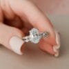 Oval Engagement Ring with Wedding Band Set A woman's hand wearing a 2.5-carat oval cut moissanite engagement ring and a matching wedding band. The engagement ring features a braided diamond band an