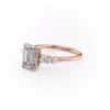 Close-up of classic emerald cut moissanite centre stone in four claw setting rose gold engagement ring with cluster shoulders